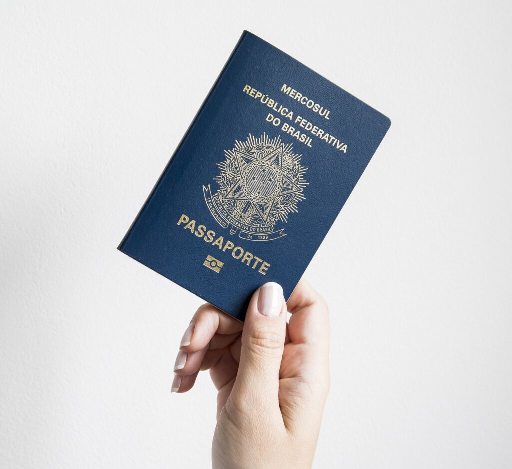 Passaporte brasileiro azul sendo segurado por uma mão feminina com unhas claras, destacando a importância do documento e da autorização de viagem para menores em viagens internacionais.