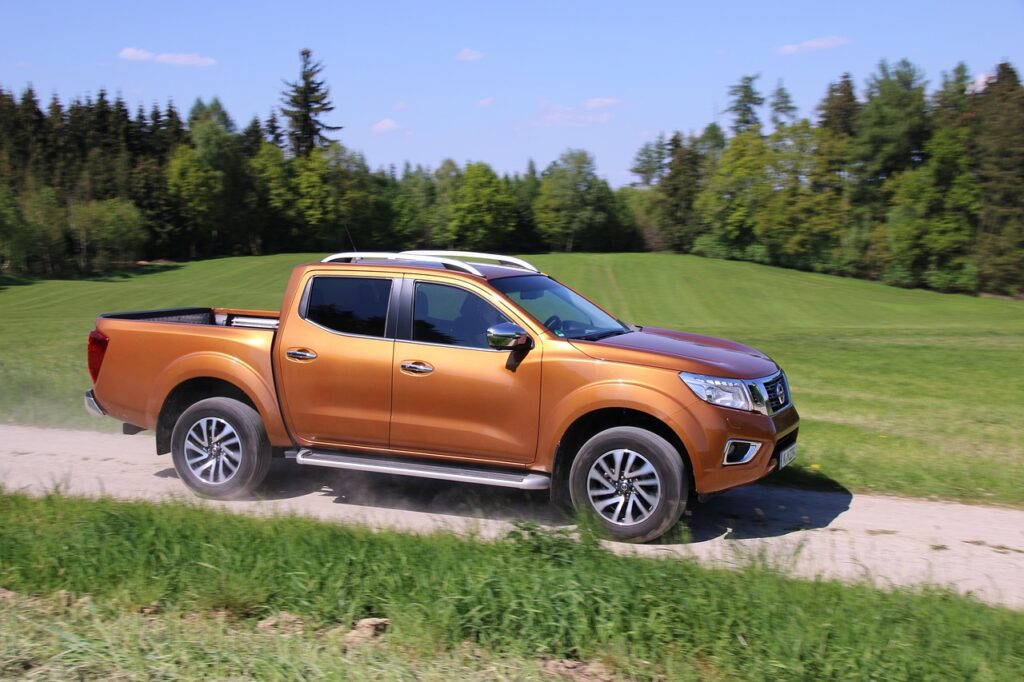 Caminhonete Nissan Frontier na cor cobre, dirigindo em alta velocidade em uma estrada de terra com paisagem rural e verde ao fundo.