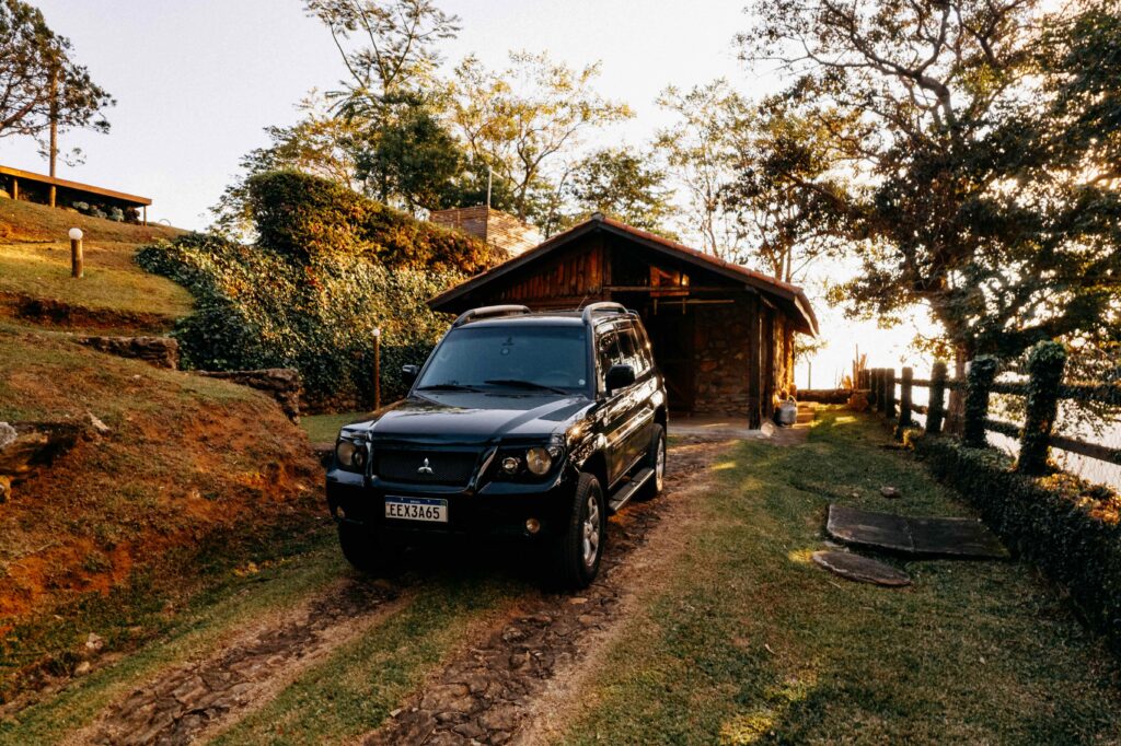 Carro 4x4 preto estacionado em frente a uma casa de campo de madeira em um final de tarde, com a luz do sol nas árvores ao fundo.