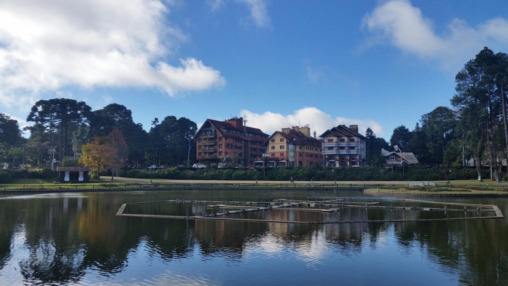 Vista panorâmica do Lago Capivari, com edifícios de arquitetura europeia e telhados inclinados refletidos na água, na Vila Capivari, principal centro turístico de Campos do Jordão.