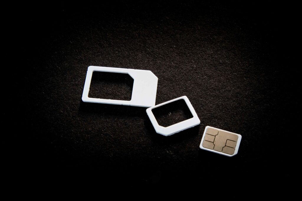 Três tipos de cartões SIM dispostos sobre um fundo preto. A imagem mostra um chip SIM completo e, ao lado dele, os adaptadores para os formatos micro SIM e nano SIM.