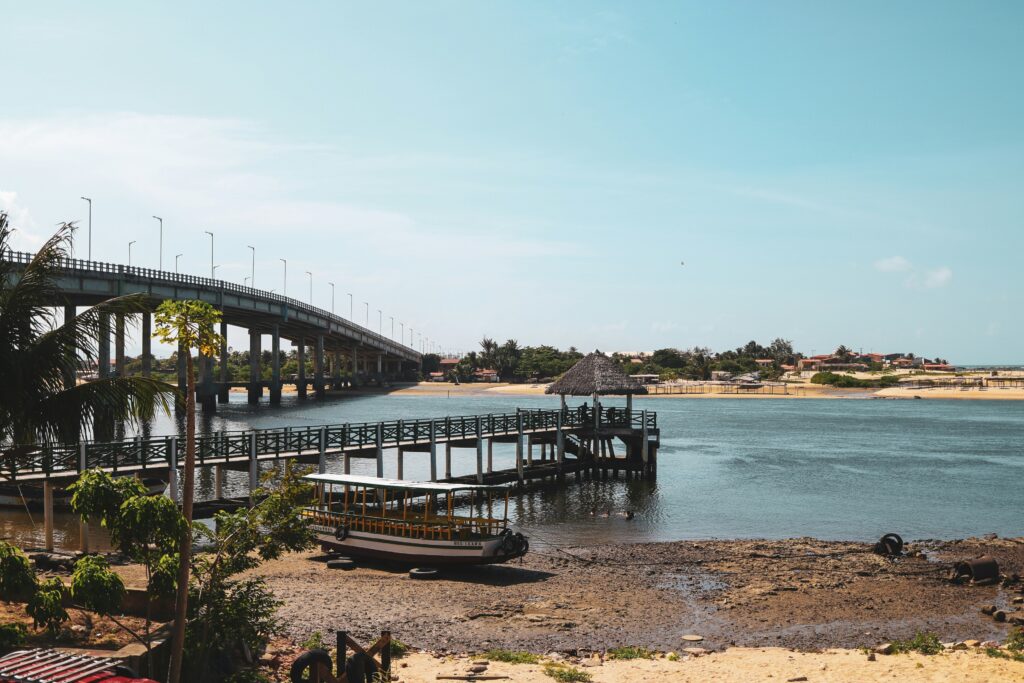 Ponte de concreto sobre o rio ou estuário em Cumbuco, próximo a Fortaleza, com um deck de madeira, quiosque rústico e um barco de passeio ancorado na maré baixa.